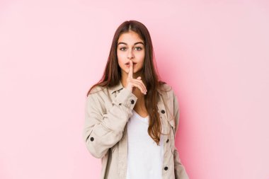 Pembe arka planda poz veren genç beyaz kadın ya sır saklıyor ya da sessizlik istiyor..