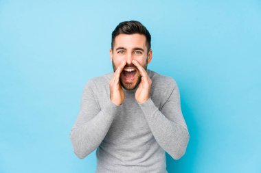 Young caucasian man against a blue background isolated shouting excited to front.