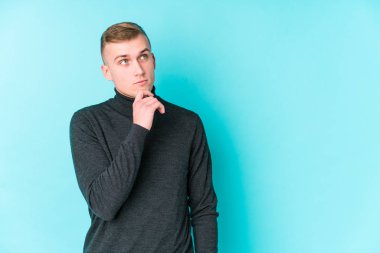 Mavi arka planda beyaz bir adam şüpheli ve şüpheci bir ifadeyle yana bakıyor..