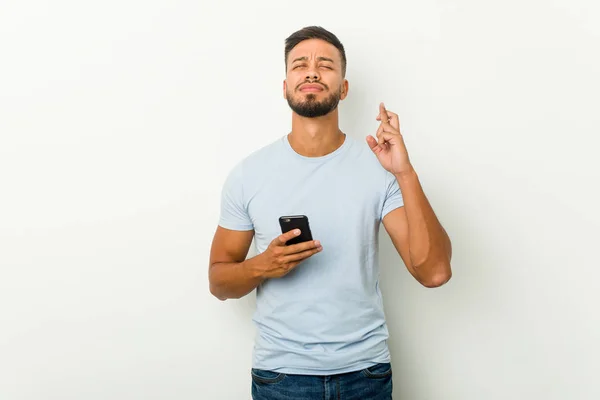 Jovem Mestiço Asiático Homem Segurando Telefone Cruzando Dedos Para Ter — Fotografia de Stock