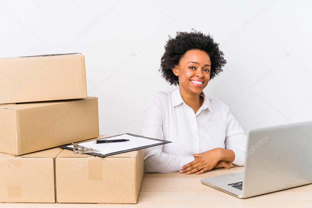 Warehouse manager sitting checking deliveries with laptop looks aside smiling, cheerful and pleasant.