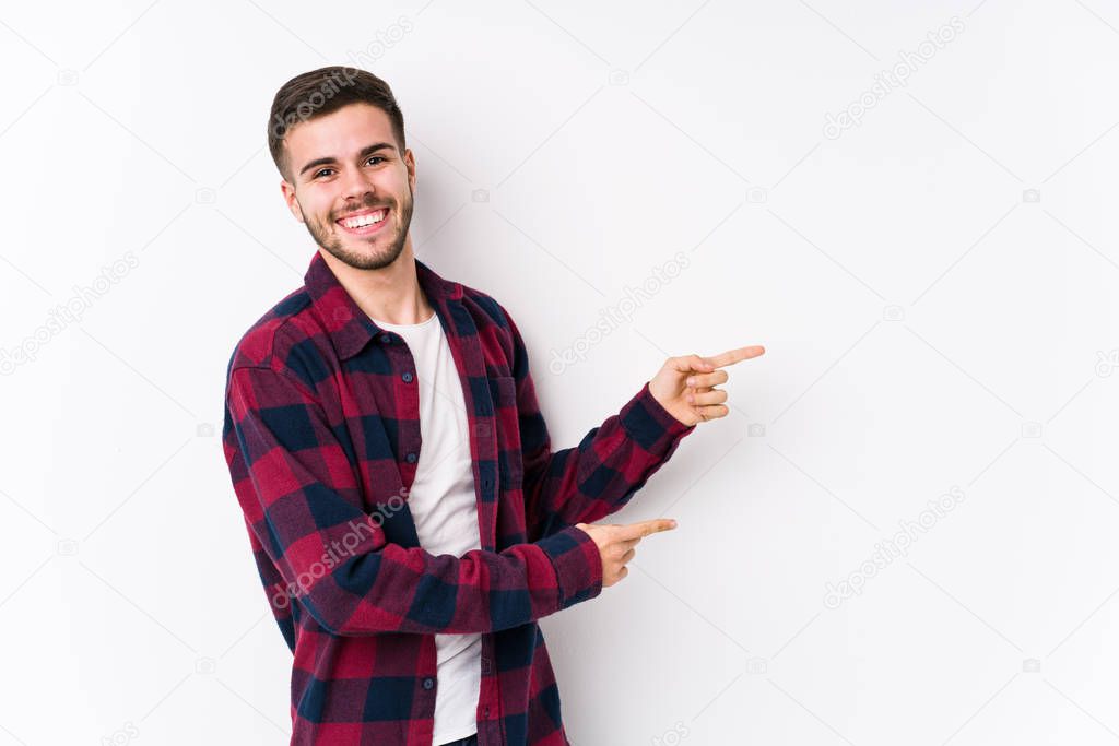 Young caucasian man posing in a white background isolated excited pointing with forefingers away.