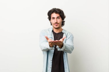 Beyaz arka planda genç yakışıklı bir adam elinde avuç içi bir şeyle kameraya sunuyor..