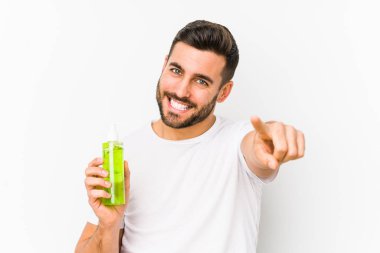 Kafkasyalı genç bir adam elinde aloe vera ile nemlendirici tutarken izole edilmiş neşeli gülümsemeler ön tarafı işaret ediyor..