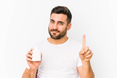 Elinde vitamin şişesi tutan genç beyaz bir adam bir numarayı parmağıyla gösteriyor..