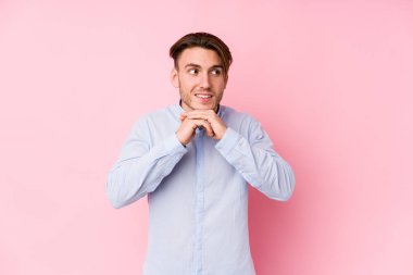 Pembe arka planda poz veren genç beyaz adam ellerini çenesinin altında tutuyor ve mutlu bir şekilde yan tarafa bakıyor..