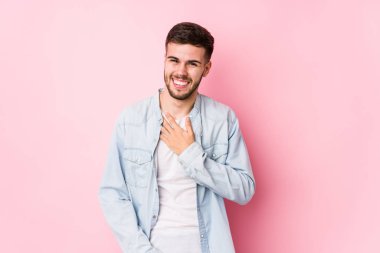 Beyaz arka planda poz veren beyaz tenli genç iş adamı kahkahalar atıyor ve elini göğsüne koyuyor. 