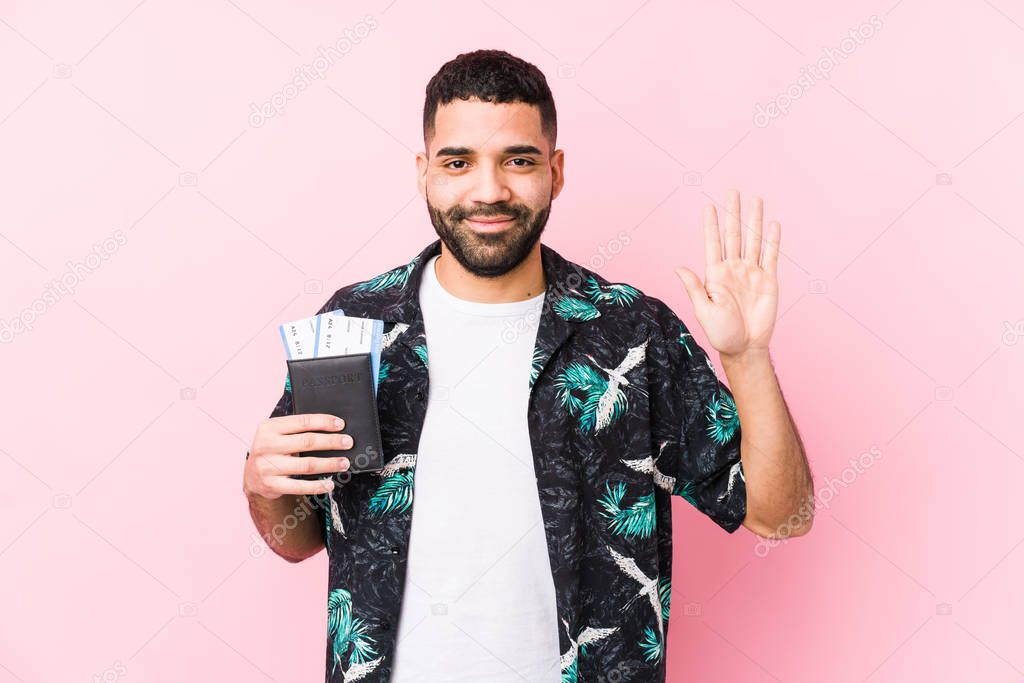 Young arabian cool man holding a boarding passes isolated smiling cheerful showing number five with fingers.