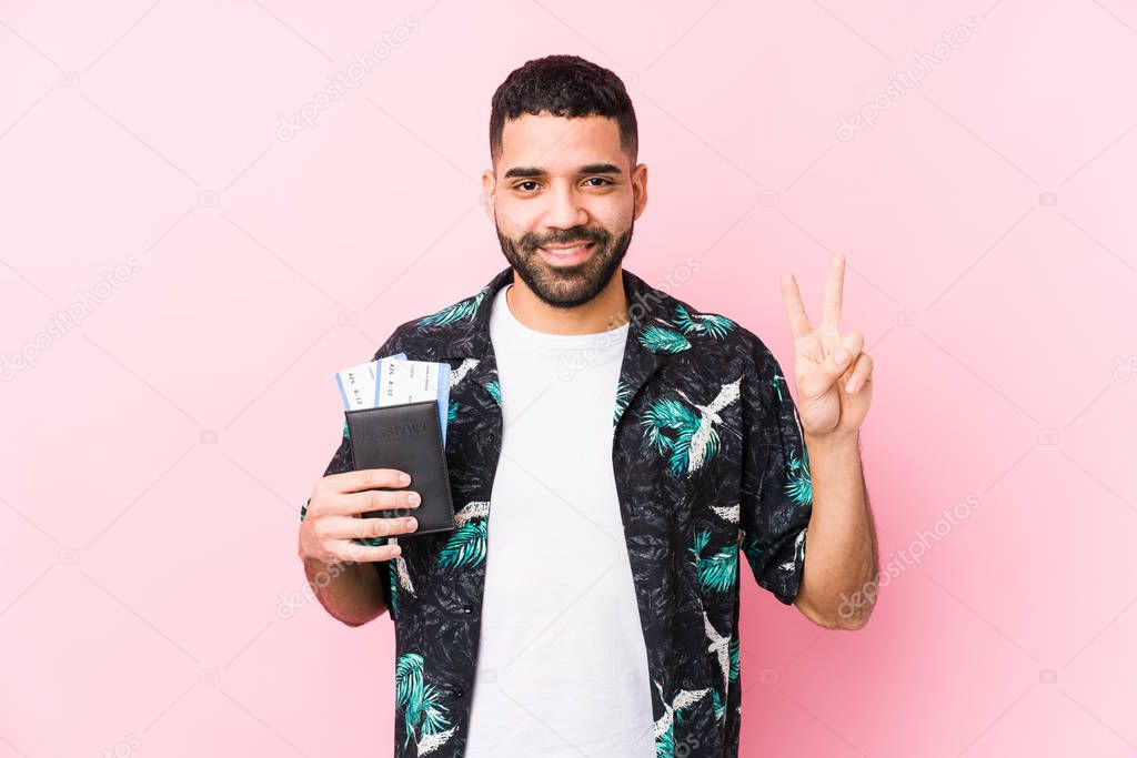 Young arabian cool man holding a boarding passes isolated showing number two with fingers.