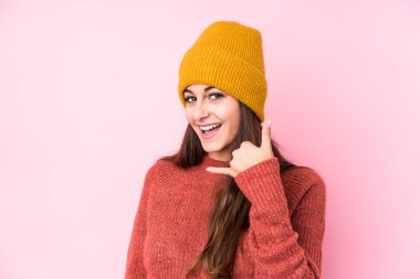 Yün şapka takan genç beyaz kadın cep telefonu hareketini parmaklarıyla gösteriyor..