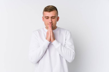 Beyaz arka planda el ele tutuşan beyaz tenli genç bir adam ağzına yakın dua ediyor, kendinden emin..