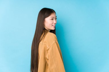 Mavi arka planda poz veren genç Çinli kadın, yalnız, gülümseyen, neşeli ve hoş bakışlar bir yana..