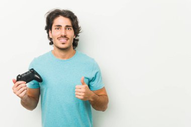 Elinde oyun kumandası tutan genç adam gülümsüyor ve başparmağını kaldırıyor.