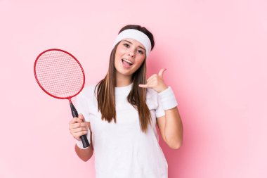 Badminton oynayan beyaz bir kadın izole edilmiş, parmaklarıyla bir cep telefonu hareketi gösteriyor..