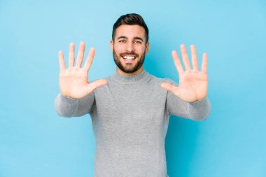 Mavi arka planda genç beyaz bir adam 10 numarayı elleriyle gösteriyor..
