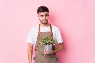 Kafası karışmış ve kendinden emin olmayan bir bitkiyi elinde tutan beyaz bir bahçıvan..