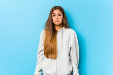 Young sporty woman shrugs shoulders and open eyes confused.