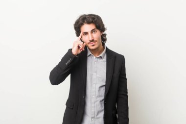 Genç bir iş adamı beyaz bir zemine karşı parmağıyla tapınağı işaret ediyor, düşünüyor ve bir göreve odaklanıyor..