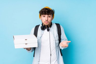 Elinde pizza tutan genç Arap öğrenci omuz silkiyor ve gözleri açık..