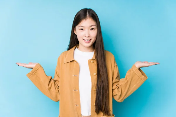 Young Chinese Woman Posing Blue Background Isolated Makes Scale Arms — Stock Photo, Image