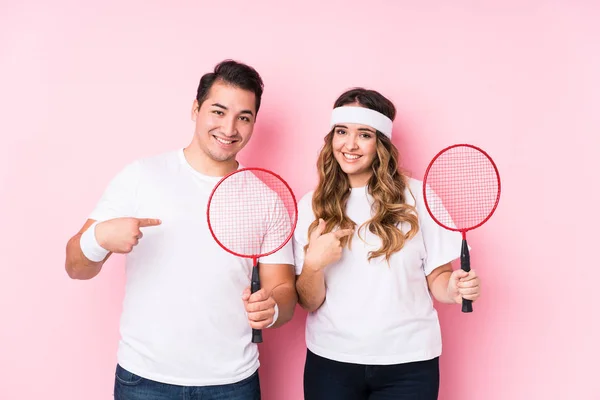 Young couple playing badminton isolated person pointing by hand to a shirt copy space, proud and confident