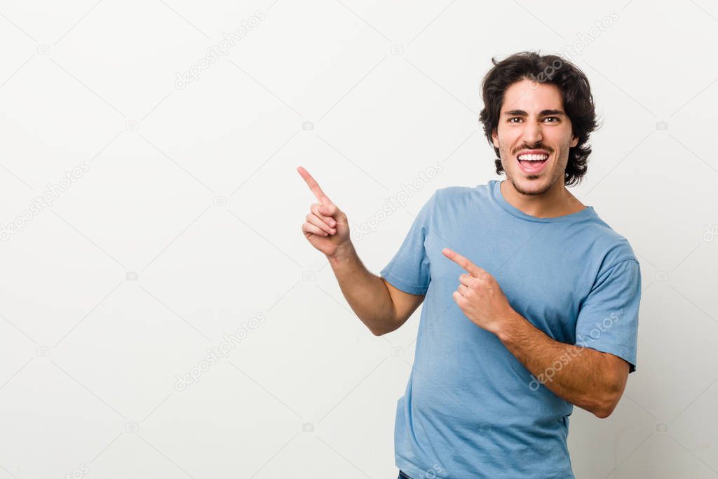 Young handsome man against a white background pointing with forefingers to a copy space, expressing excitement and desire.