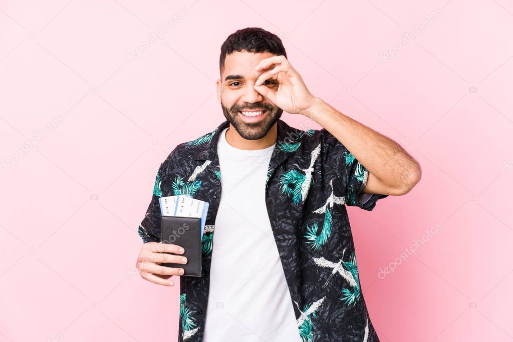 Young arabian cool man holding a boarding passes isolated excited keeping ok gesture on eye.