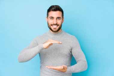 Mavi arka planda genç beyaz adam iki eliyle bir şey tutuyor, ürün sunumu..