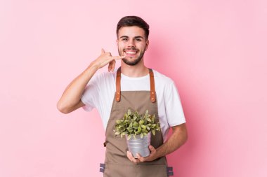 Kafkas 'lı genç bahçıvan elinde bir bitki tutuyor ve parmaklarıyla bir cep telefonu hareketi gösteriyor..