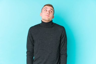 Mavi arka plandaki genç beyaz adam hedeflere ve amaçlara ulaşmayı hayal ediyor.