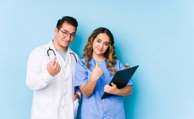 Mavi arka planda poz veren genç doktor çift, sanki sizi davet ediyormuş gibi parmakla işaret ediyor..