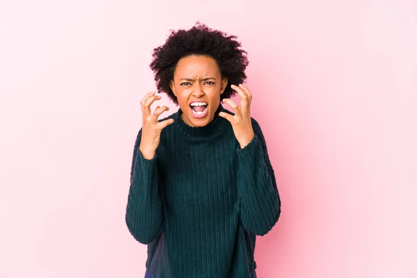 Middle aged african american woman against a pink background isolated upset screaming with tense hands.