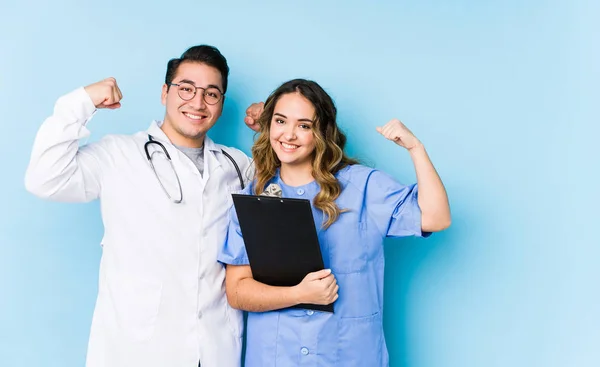 Young Doctor Couple Posing Blue Background Isolated Showing Strength Gesture — 스톡 사진