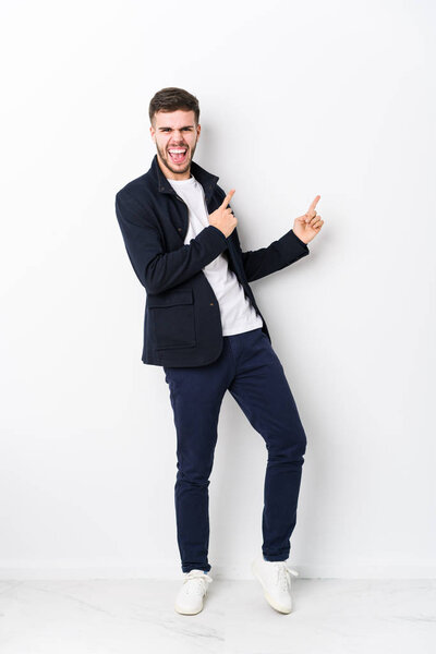 Full body young caucasian man isolated pointing with forefingers to a copy space, expressing excitement and desire.