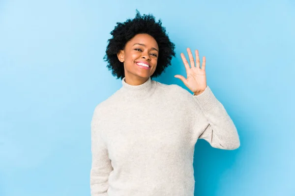 中年アフリカ系アメリカ人女性に対して青の背景隔離された笑顔陽気に示す番号5とともに指 — ストック写真