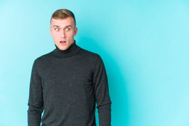 Mavi arka plandaki genç beyaz adam gördüğü bir şey yüzünden şoka uğruyor..