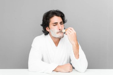 Gri bir arka planda sakalını kesen genç beyaz bir adam.