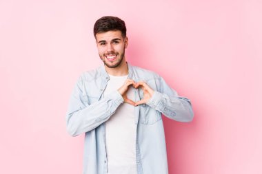 Beyaz arka planda poz veren beyaz tenli genç bir iş adamı izole edilmiş gülümsüyor ve elleriyle kalp şeklini gösteriyor.. 