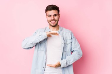 Beyaz arka planda poz veren beyaz tenli genç bir iş adamı iki eliyle bir şey tutuyor..