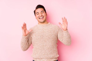 Pembe arka planda poz veren kıvrımlı genç adam neşeli bir şekilde gülüyor. Mutluluk kavramı.