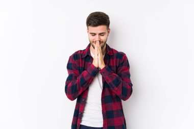 Beyaz arka planda poz veren beyaz tenli genç bir adam yalnız başına el ele tutuşup dua ediyor, kendinden emin hissediyor..