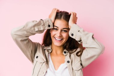 Pembe arka planda poz veren beyaz bir kadın ellerini başının üstünde tutarak gülüyor. Mutluluk kavramı.