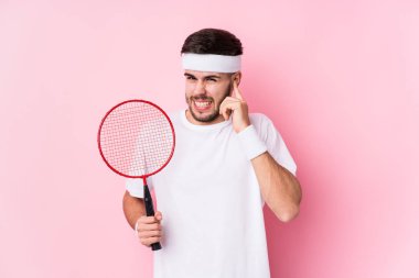 Badminton oynayan beyaz bir adam elleriyle kulaklarını kapatıyor..