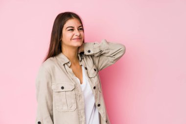 Pembe arka planda poz veren beyaz bir kadın kafasının arkasına dokunuyor, düşünüyor ve bir seçim yapıyor..