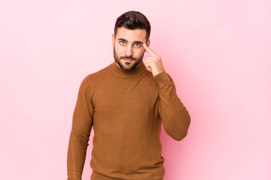 Pembe arka planda genç beyaz bir adam. Bir tapınağı işaret ediyor, düşünüyor ve bir göreve odaklanıyor..