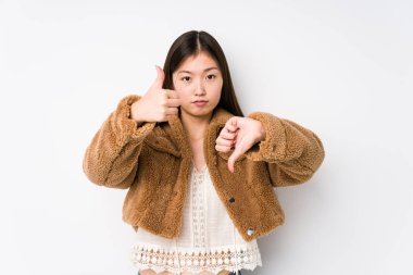 Beyaz arka planda poz veren Çinli genç bir kadın. Onaylıyor ve baş parmağını aşağı gösteriyor. Zor seçim konsepti.