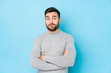 Mavi arka planda genç, beyaz bir adam yalnız başına kameraya alaycı bir ifadeyle bakıyor..