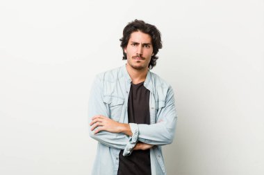 Beyaz bir arka planı olan, hoşnutsuzca kaşlarını çatan, kollarını kavuşturan genç yakışıklı bir adam..