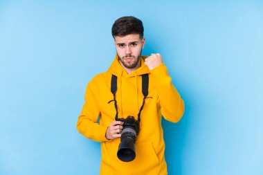 Kafkasyalı genç fotoğrafçı kameraya yumruk gösteriyor, agresif bir yüz ifadesi var..