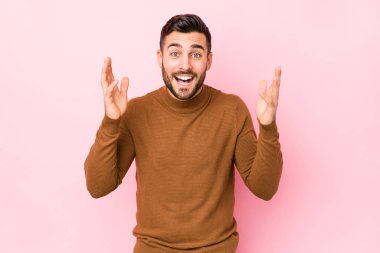 Pembe arka planda yaşayan beyaz bir genç hoş bir sürprizle karşılaşıyor, heyecanlı ve el kaldırıyor..